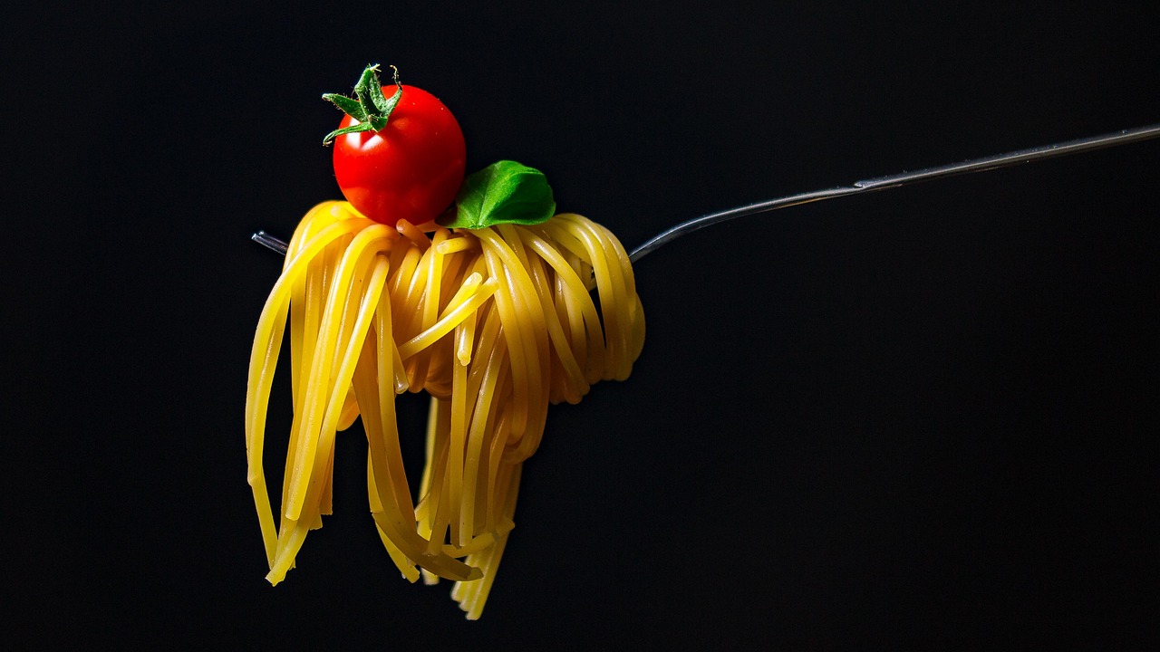 Una ciotola di pasta con sugo, accompagnata da verdure fresche e spezie.